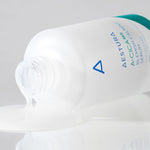 A partially spilled bottle of Aestura A-Cica 365 Blemish Calming Serum with its clear, smooth serum pooling on a reflective surface.