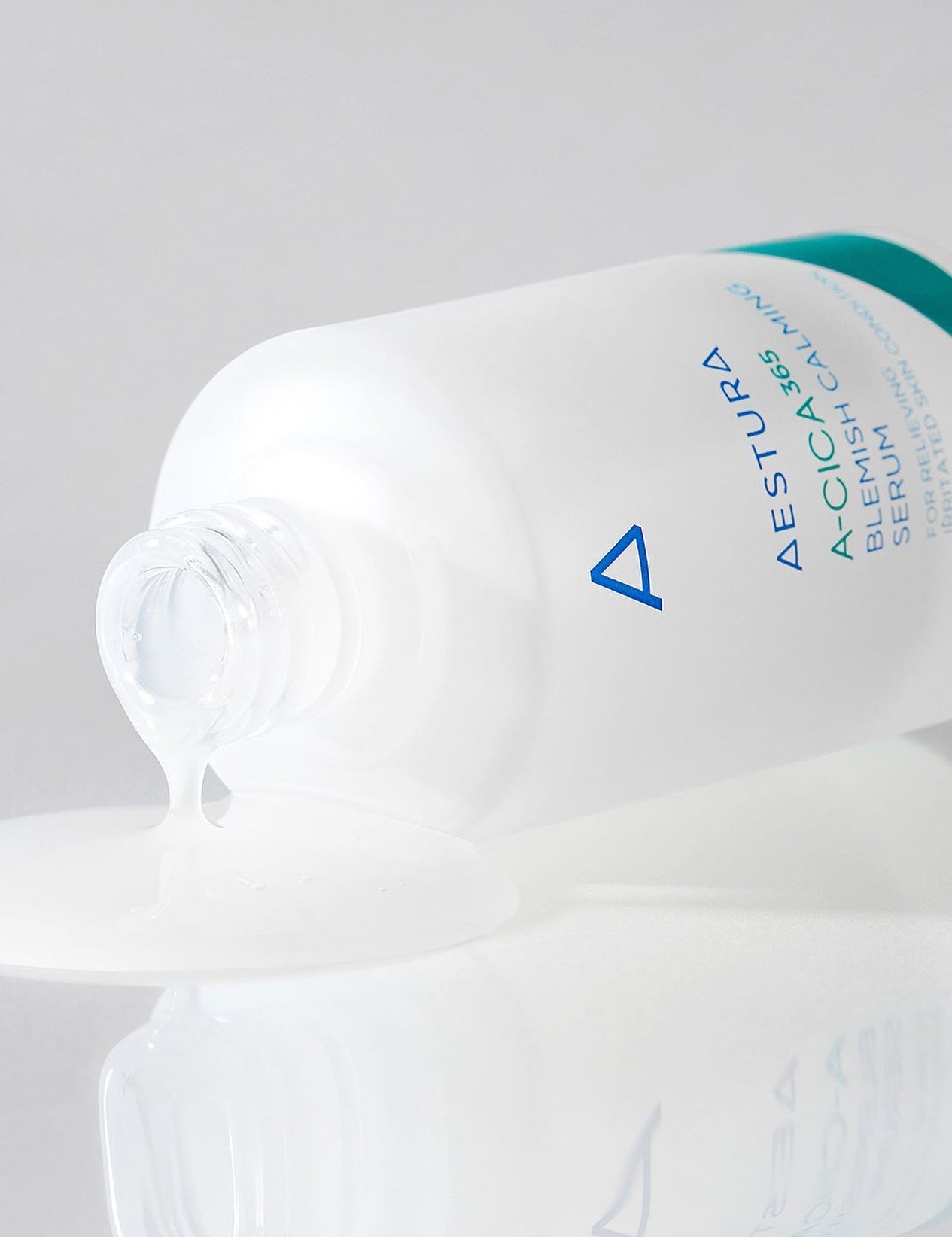 A partially spilled bottle of Aestura A-Cica 365 Blemish Calming Serum with its clear, smooth serum pooling on a reflective surface.