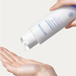 A hand dispensing milky-light hydrating essence from an Aestura Atobarrier 365 Hydro Essence bottle onto another hand, set against a light background.