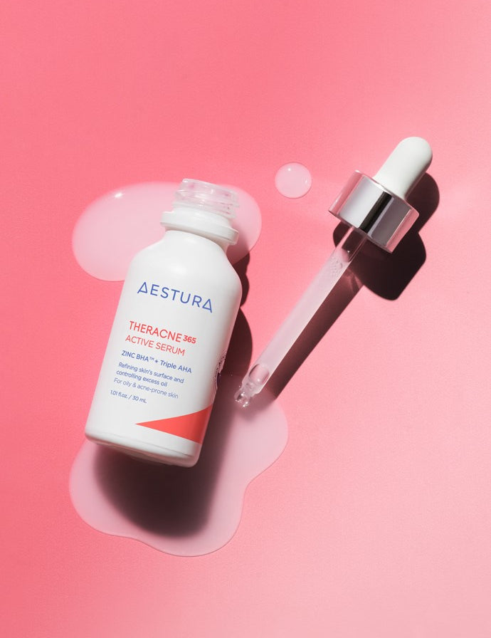 A bottle of Aestura Theracne 365 Active Serum with a dropper, resting on a soft pink surface, with serum pooling beneath.