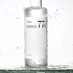 A clear bottle of Anua Heartleaf 77% Soothing Toner, splashed with water droplets, set against a minimalist white background.
