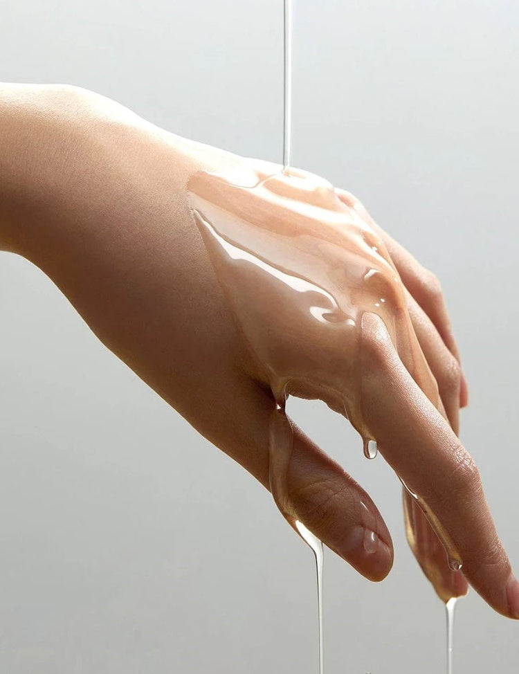 A hand with Anua Heartleaf Pore Control Cleansing Oil dripping off, illustrating its texture and fluidity against a light background.