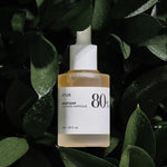 A bottle of Anua Heartleaf Soothing Ampoule surrounded by green heartleaf leaves, showcasing its natural skincare appeal.