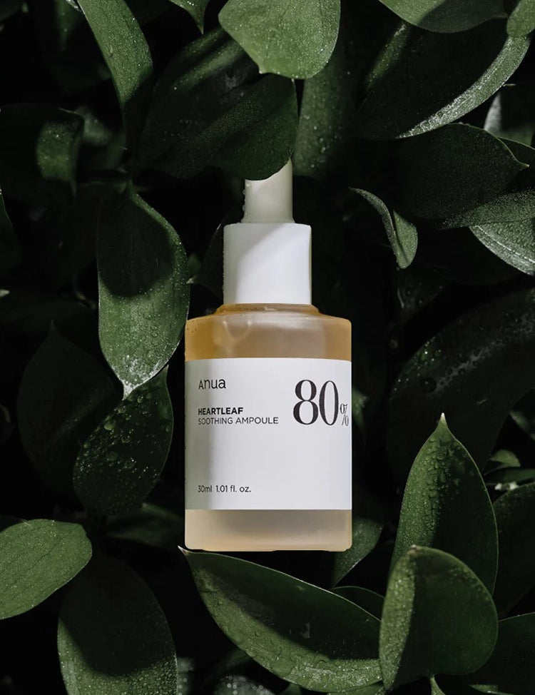 A bottle of Anua Heartleaf Soothing Ampoule surrounded by green heartleaf leaves, showcasing its natural skincare appeal.