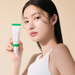 A model with long black hair holds Axis-Y Dark Spot Correcting Glow Serum against a light beige background, showcasing the product’s design.