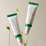 Two tubes of Axis-Y Dark Spot Correcting Glow Serum with green lids, displayed with delicate flowers on a beige background.
