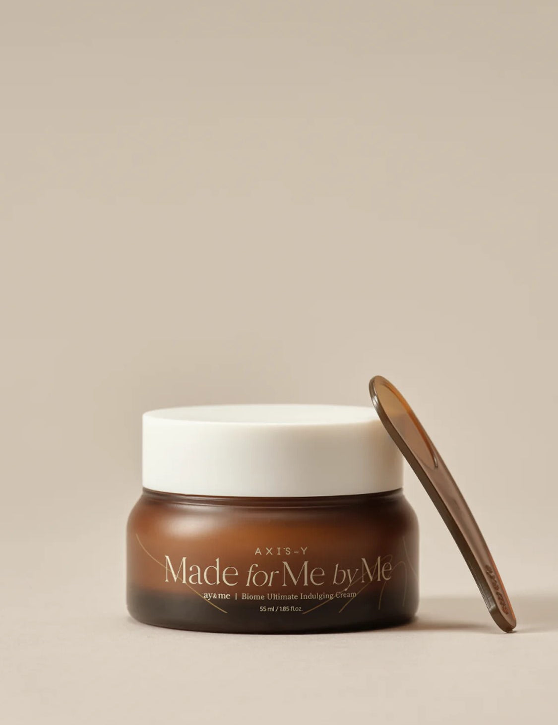 Brown jar of AXIS-Y 'Made for Me by Me' Biome Ultimate Indulging Cream with white lid and brown spatula, set against a beige background.