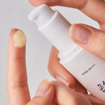 A close-up of a hand dispensing Beauty of Joseon Ginseng Moist Sun Serum onto a fingertip, showcasing its smooth, creamy texture.