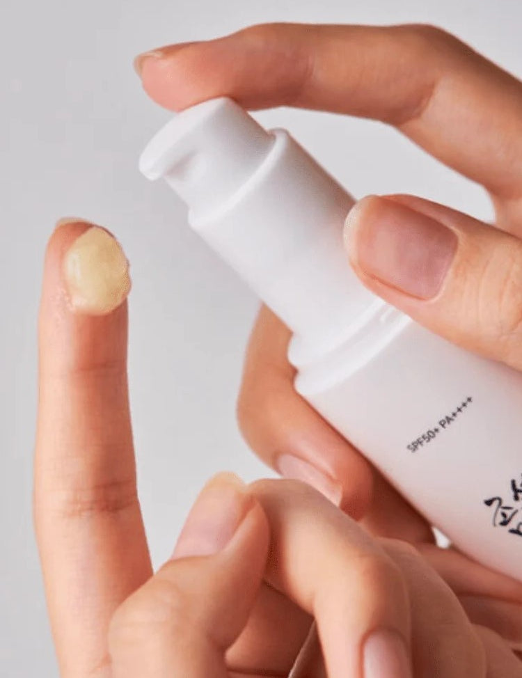 A close-up of a hand dispensing Beauty of Joseon Ginseng Moist Sun Serum onto a fingertip, showcasing its smooth, creamy texture.
