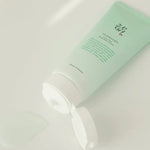 Beauty of Joseon Green Plum Refreshing Cleanser lying on a reflective surface with the cap open and a small amount of light gel texture oozing out, showcasing its refreshing formula.