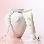 Beauty of Joseon Relief Sun: Rice + Probiotics leaning against a white vase, surrounded by pearls and cosmetic particles on a soft pink background, highlighting its elegant design and skincare benefits.