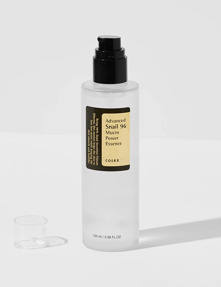 A bottle of Cosrx Advanced Snail 96 Mucin Power Essence with a black pump beside its small transparent cap on a light background.