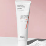 A tube of Cosrx Comfort Ceramide Cream stands on a white surface against a soft pink backdrop, highlighting its minimalist design.