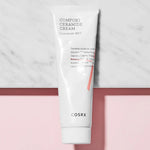 A tube of Cosrx Comfort Ceramide Cream, featuring a minimalist design, sits on a marble surface against a pink background.