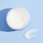 Cosrx Hyaluronic Acid Intensive Cream on a pastel blue surface, with a small blob of cream showcasing its smooth texture.