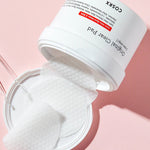 A white jar of COSRX Original Clear Pad with cotton pads partially pulled out, resting on a pink background.