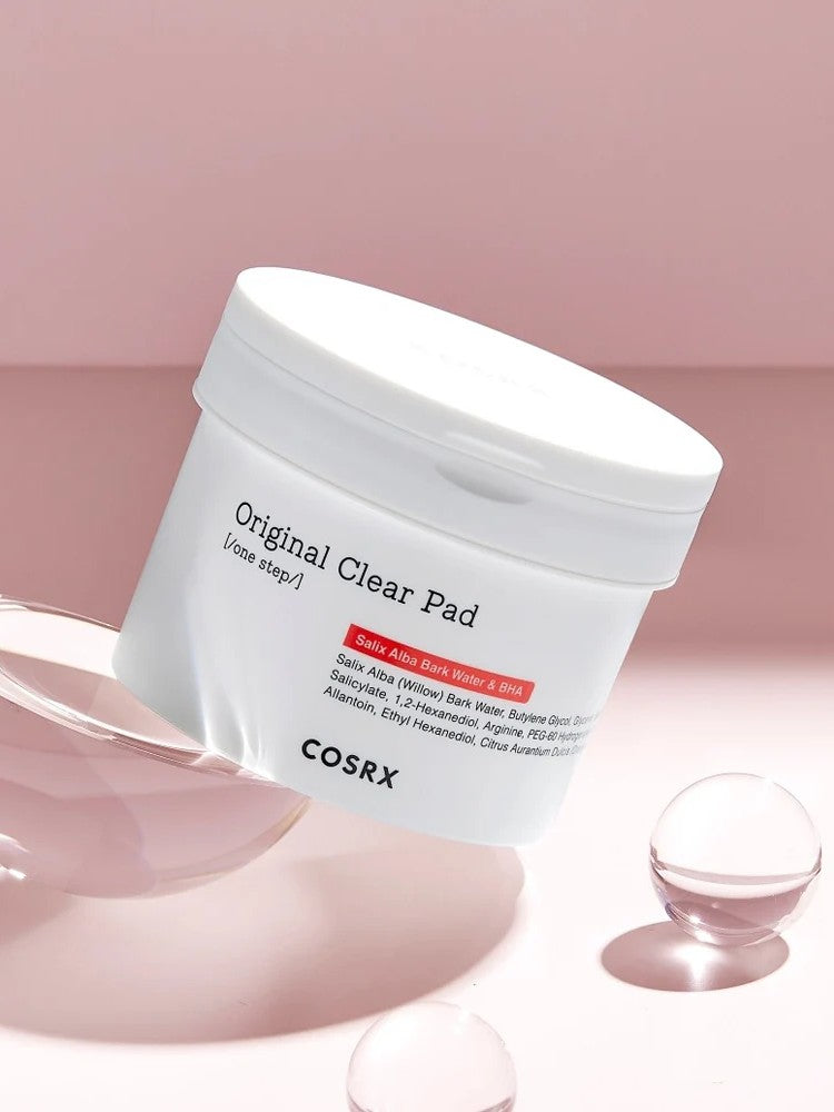 A container of COSRX Original Clear Pad on a pink background, highlighting skincare ingredients like Salix Alba Bark Water and BHA.