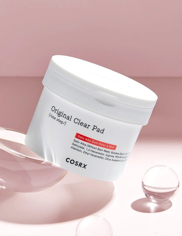 A container of COSRX Original Clear Pad on a pink background, highlighting skincare ingredients like Salix Alba Bark Water and BHA.