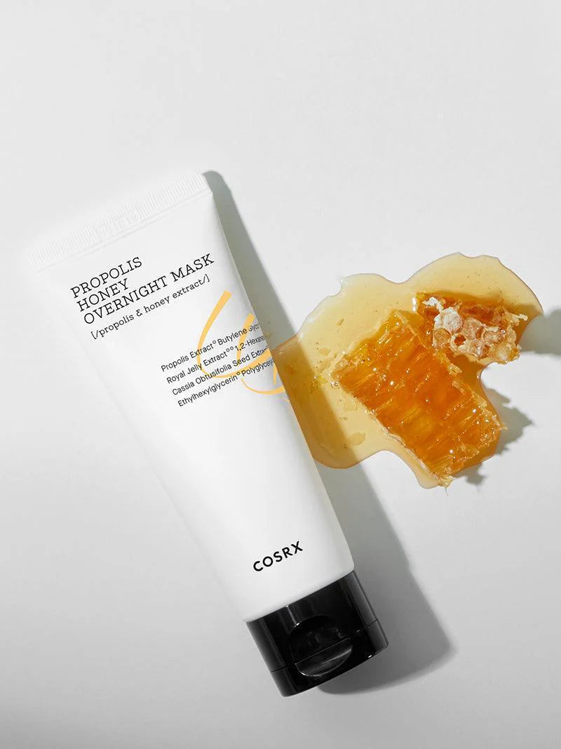 Cosrx Propolis Honey Overnight Mask tube beside a drip of honey and honeycomb, set against a white background, emphasizing its nourishing and honey-infused formula.