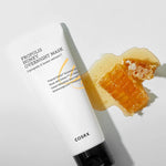 Cosrx Propolis Honey Overnight Mask tube beside a drip of honey and honeycomb, set against a white background, emphasizing its nourishing and honey-infused formula.