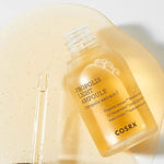 Cosrx Propolis Light Ampoule with dropper, surrounded by its golden, viscous texture resembling honey, highlighting its nourishing and soothing properties.