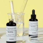 Two black bottles of Cosrx The Vitamin C 23 Serum on a yellow background, paired with glass beakers and pipettes, evoking skincare preparation.