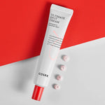 A tube of Cosrx Ultimate Spot Cream with a red cap, placed on a red and white background, alongside small dollops of cream.