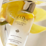 A bottle of d'Alba First Spray Serum with a silver cap, submerged in water, highlighting its dual-layer oil and serum formula.