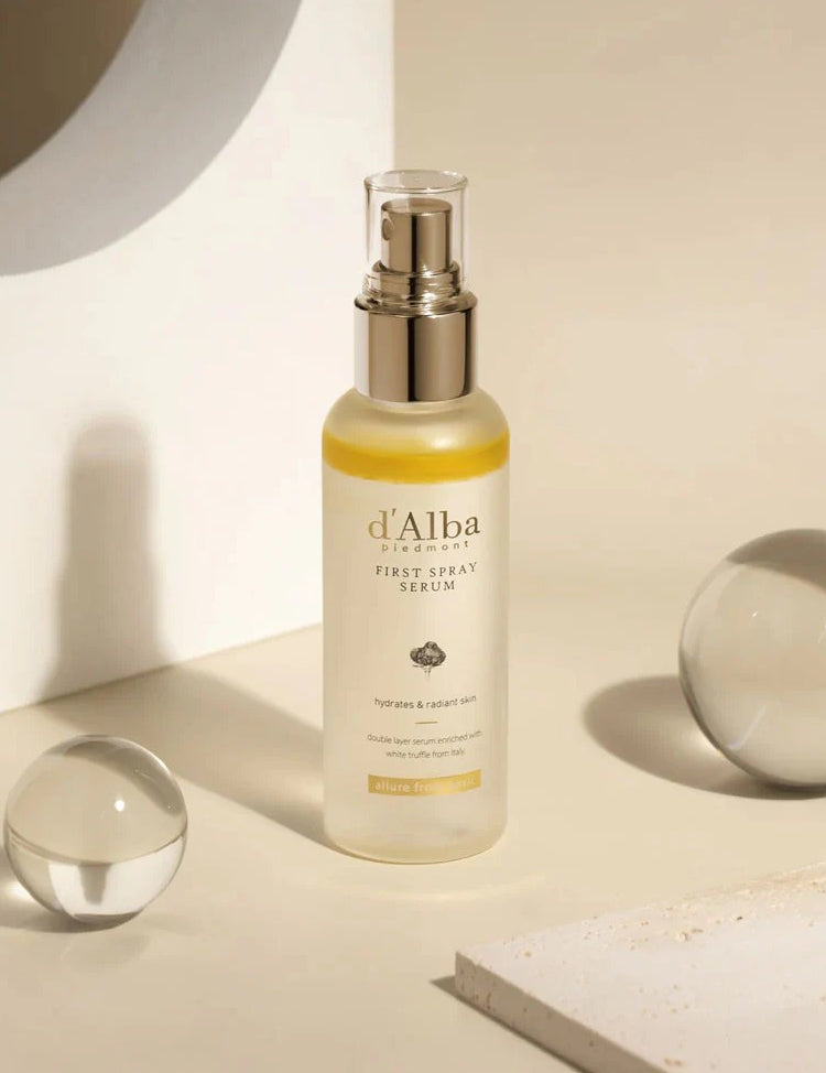 A bottle of d'Alba First Spray Serum on a minimalist surface with glass spheres, emphasizing hydration and radiance.