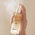 A hand holds a d'Alba First Spray Serum bottle, releasing a fine mist to highlight its hydrating and radiance-boosting benefits.