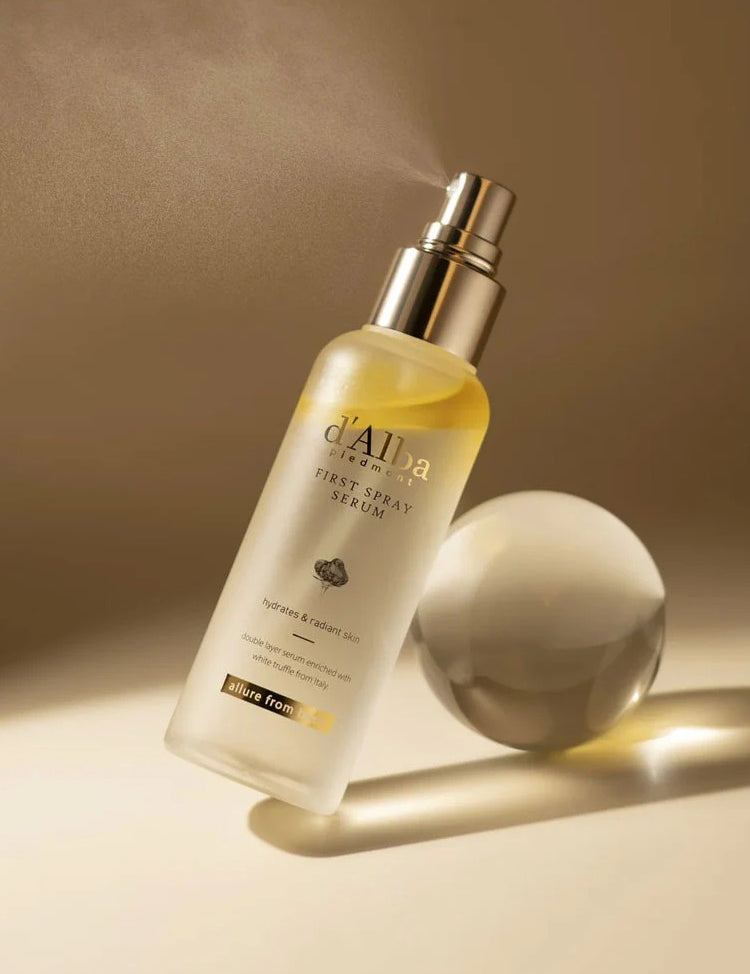 A sleek bottle of d'Alba First Spray Serum with a mist nozzle, set against a soft beige background to evoke luxury and hydration.