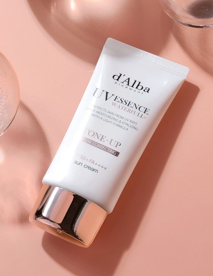 A tube of d'Alba UV Essence Waterfull Sun Cream on a pink surface, highlighting its tone-up and moisturizing formula for radiant, hydrated skin.