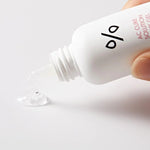 A hand holding a bottle of Dr. Ceuracle AC Cure Solution Pink Gel, with a clear gel droplet spilling onto a plain surface, showcasing its lightweight and soothing texture.