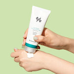 A hand squeezing Dr. Ceuracle CICA Regen Waterproof Sun Cream onto another hand against a light green background, highlighting its creamy yet lightweight texture.
