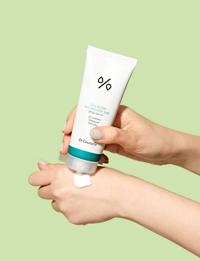 A hand squeezing Dr. Ceuracle CICA Regen Waterproof Sun Cream onto another hand against a light green background, highlighting its creamy yet lightweight texture.