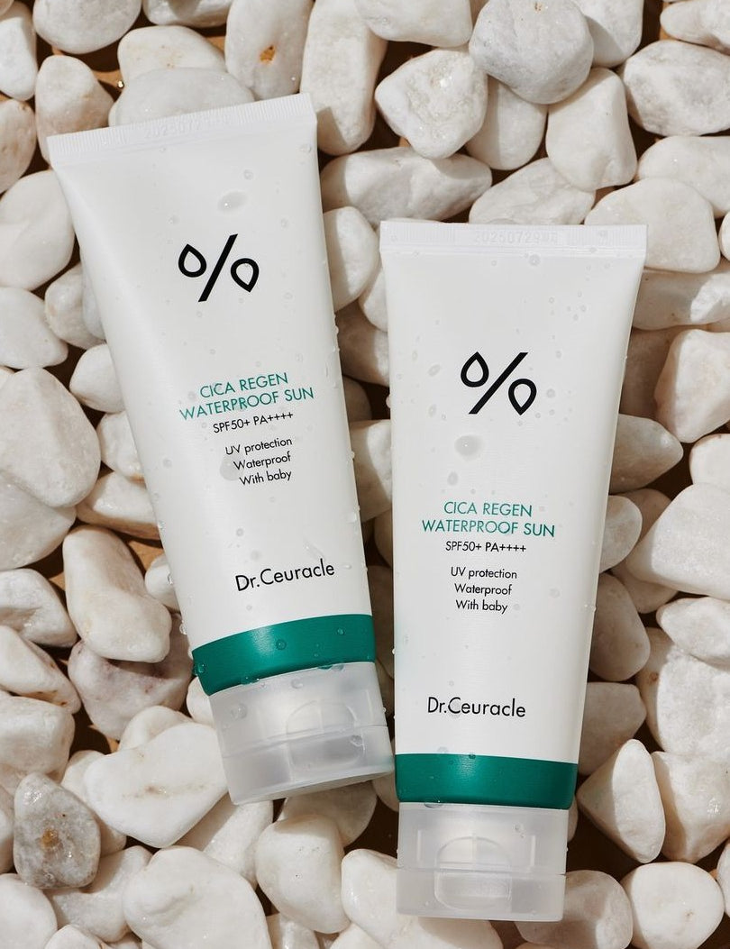 Two tubes of Dr. Ceuracle CICA Regen Waterproof Sun Cream with SPF 50+ PA++++, surrounded by white pebbles and water droplets, highlighting its waterproof formula and suitability for babies as indicated on the labels.