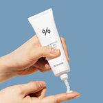 A hand holding a tube of Dr. Ceuracle sun cream, dispensing the lightweight product onto another hand against a blue background.