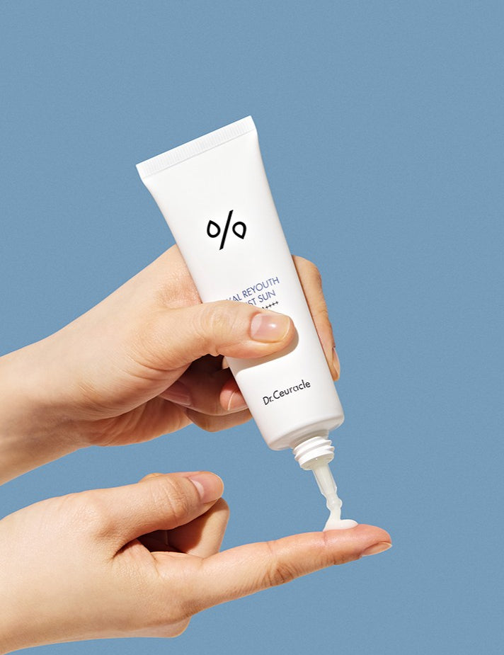 A hand holding a tube of Dr. Ceuracle sun cream, dispensing the lightweight product onto another hand against a blue background.