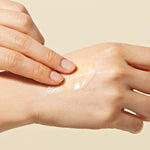 A hand applying Dr. Ceuracle Royal Vita Propolis 33 Capsule Eye Cream, featuring small Propolis beads in the texture, onto skin against a soft beige background.