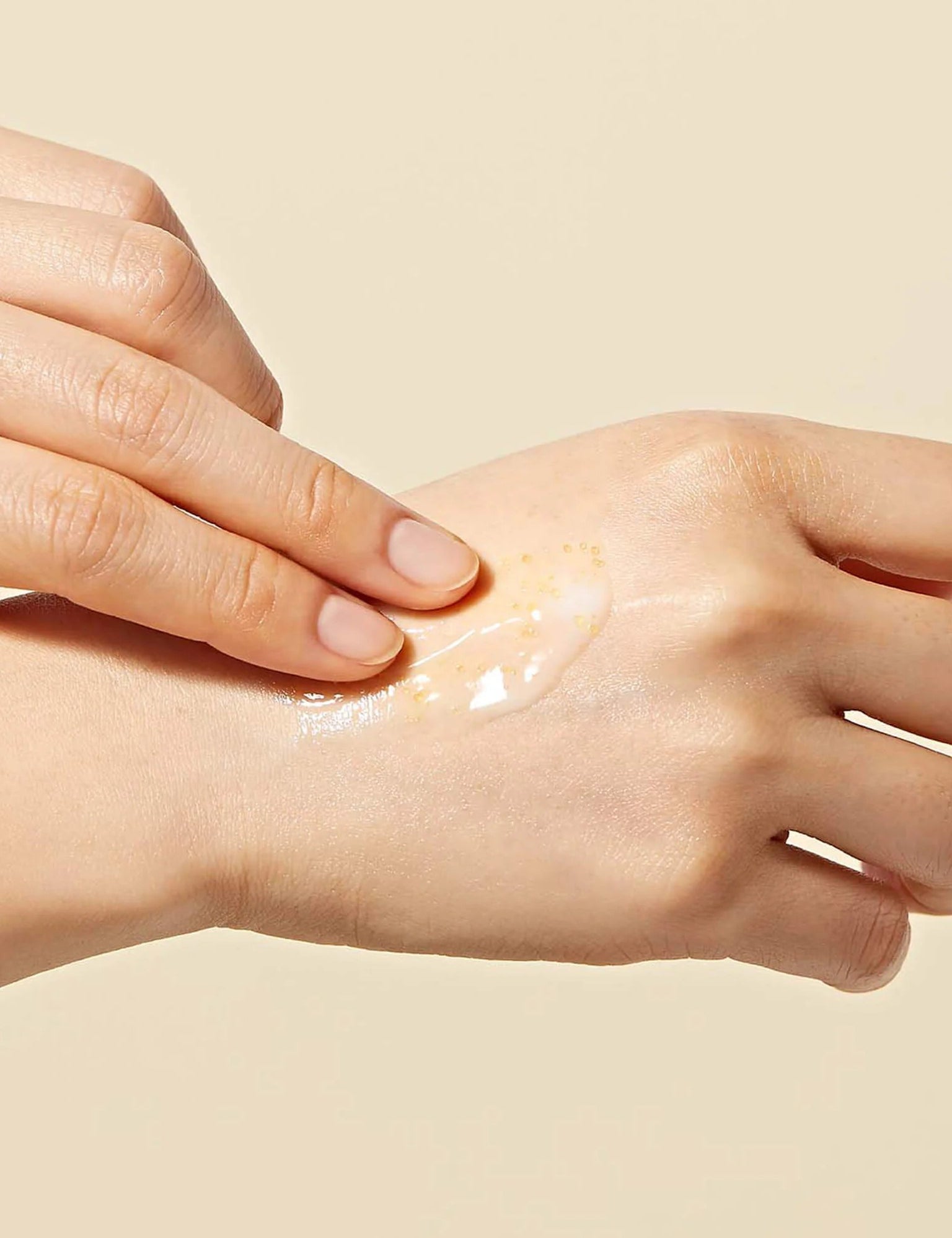 A hand applying Dr. Ceuracle Royal Vita Propolis 33 Capsule Eye Cream, featuring small Propolis beads in the texture, onto skin against a soft beige background.