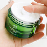 A hand dipping into a green jar of Dr. Ceuracle Tea Tree Purifine 80 Cream, showcasing its creamy texture.