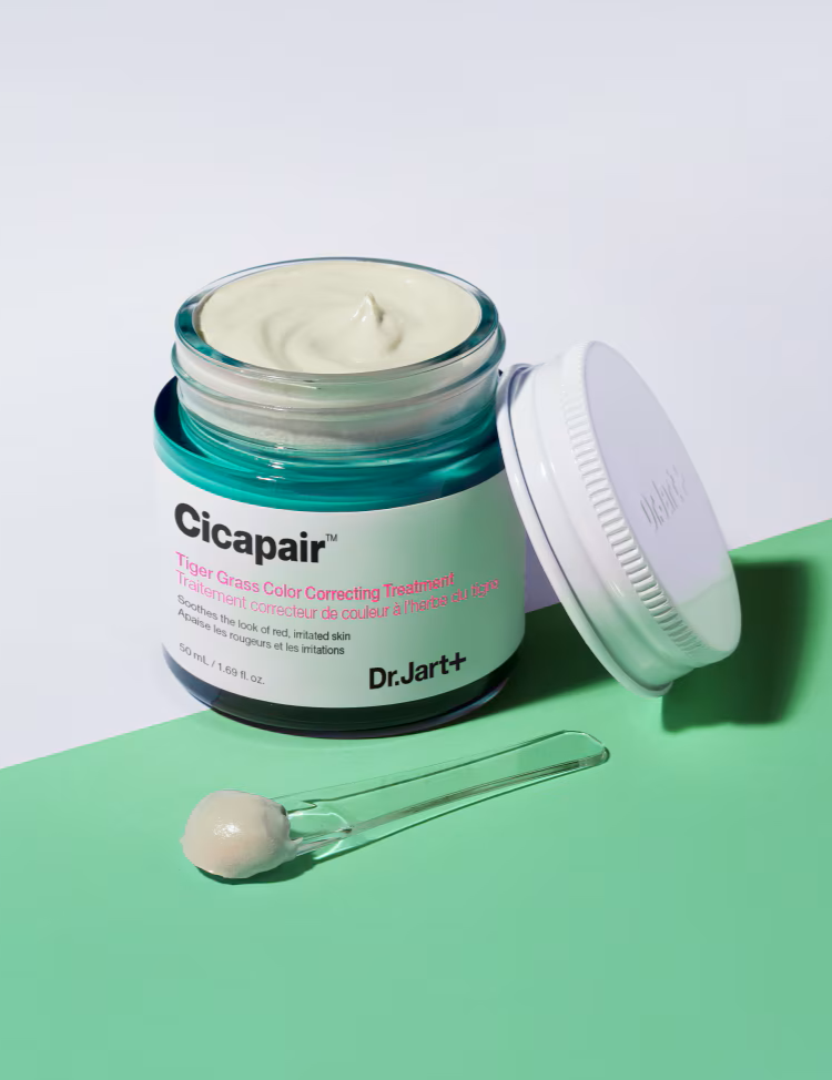 Open jar of Dr. Jart+ Cicapair Tiger Grass Color Correcting Treatment with cream on a spatula, set against a pastel background, emphasizing its smooth and soothing texture.