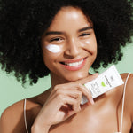 A model holding Dr.G Green Mild Up Sun+ Sunscreen, with the product applied on her cheek against a soft green background.