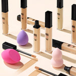 Aesthetic arrangement of Etude House Big Cover Skin Fit Concealer PRO foundation tubes, concealer wands, and pink and purple blending sponges displayed on a smooth surface.