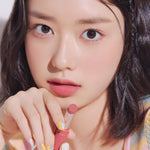 A close-up of a model holding a pink lipstick from the Etude House Fixing Tint Bar collection, showing its smooth texture on her lips against a soft background.