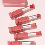 Five lipsticks from the Etude House Fixing Tint Bar collection in various pink and red shades, displayed with a clear cap labeled 'Fixing' on a soft pink background.