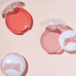 Two Etude House Lovely Cookie Blusher compacts in coral and pink, each topped with a fluffy applicator, arranged on a soft pink background.