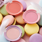 Three colorful blush compacts from the Etude House Lovely Cookie Blusher collection placed on pastel macarons, featuring peach, pink, and lavender shades against a soft pink background.