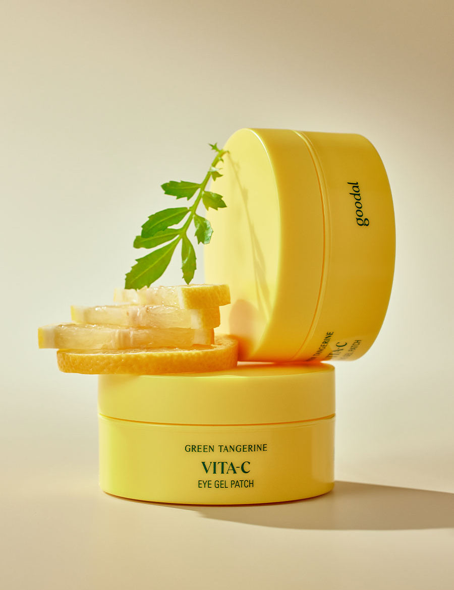 Stacked jars of Goodal Green Tangerine Vita C Eye Gel Patch, surrounded by fresh lemon slices and a green leaf, emphasizing a vibrant and refreshing skincare concept.