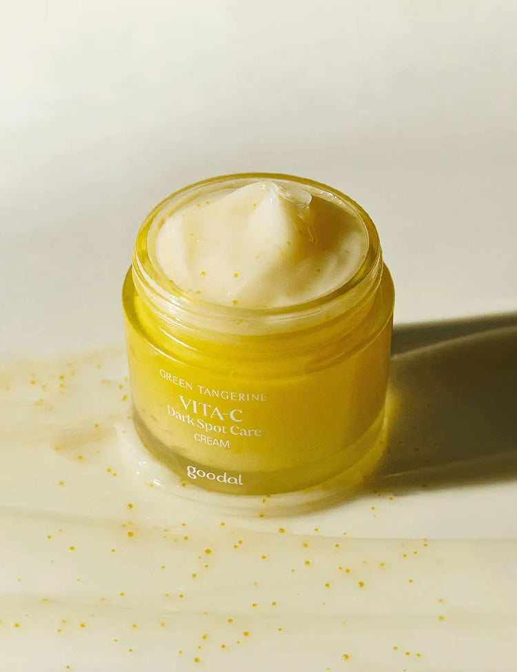 A jar of Goodal Vita-C Dark Spot Care Cream in yellow, showing its creamy texture with visible tangerine pieces, set against a light background.
